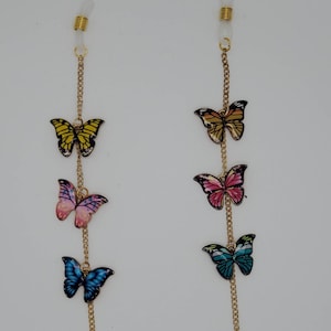 May include: A gold chain with butterfly charms in various colours, including yellow, pink, blue, and orange. The chain is designed to hold glasses.