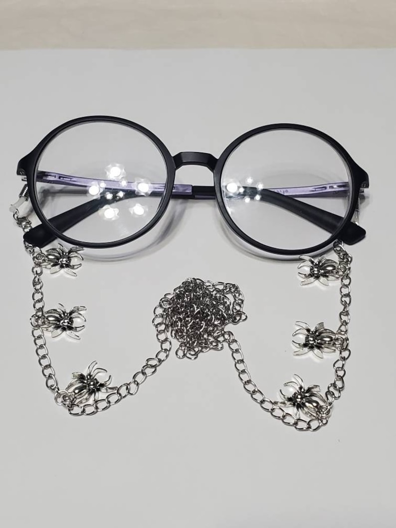 Puede incluir: Gafas redondas negras con una cadena plateada con abalorios de ara&ntilde;a.