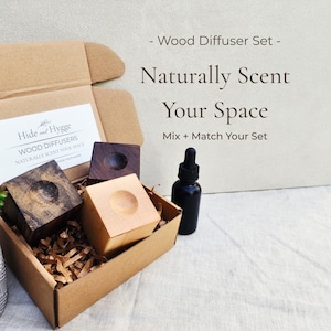Może przedstawiać: Zestaw drewnianych dyfuzorów w kartonowym pudełku, z trzema kwadratowymi drewnianymi dyfuzorami, czarną butelką z zakraplaczem i małą rośliną sukulentową w doniczce ze wzorem. Tekst na pudełku brzmi "Hide and Hygge WOOD DIFFUSERS NATURALLY SCENT YOUR SPACE". Tekst w tle brzmi "Naturally Scent Your Space".