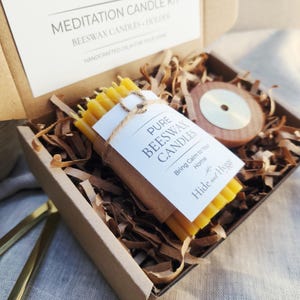 May include: A meditation candle kit in a cardboard box. The kit includes a bundle of yellow beeswax candles, a wooden candle holder, and decorative paper. The label reads "Pure Beeswax Candles" and "Bring Calm to Your Home."
