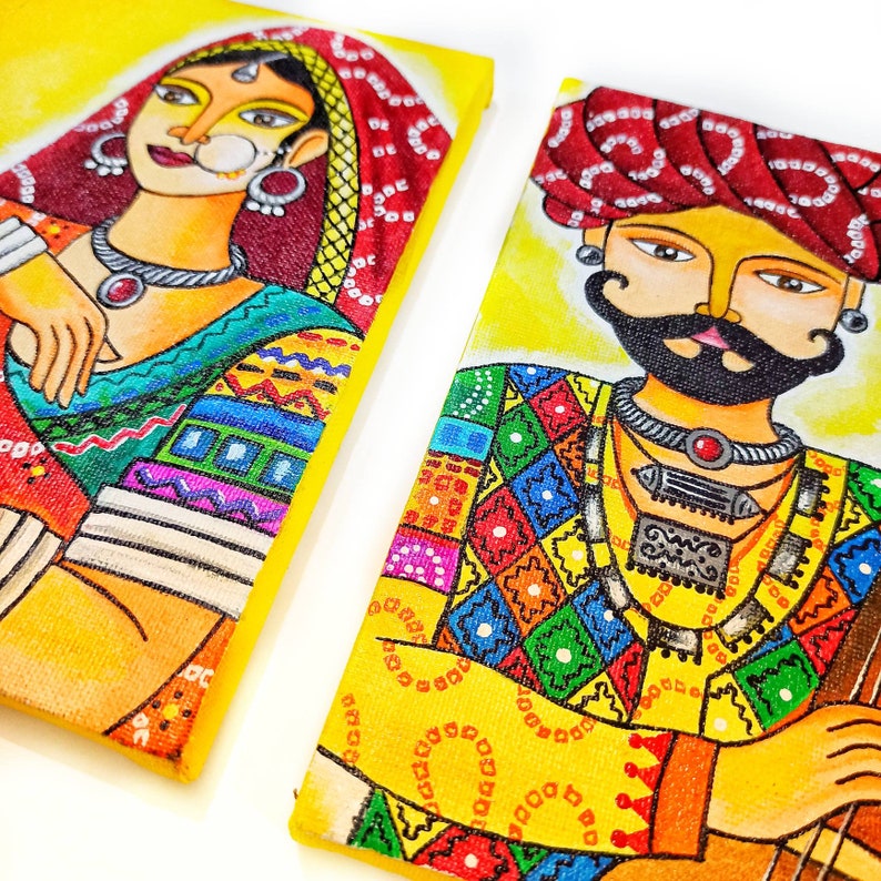 May include: Two colorful paintings on canvas featuring a woman and a man in traditional Indian clothing. The woman is wearing a red and yellow sari with intricate patterns and jewelry. The man is wearing a red turban and a colorful patterned shirt with a silver necklace. Both paintings have a yellow background.