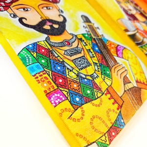 May include: A colorful painting of a man playing a stringed instrument. He is wearing a turban, a colorful shirt, and a necklace. The background is yellow.