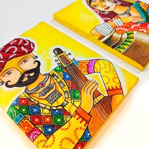 May include: Two colorful paintings on canvas depicting a man playing a stringed instrument and a woman holding a pot. The paintings are on a yellow background and feature intricate details and patterns.