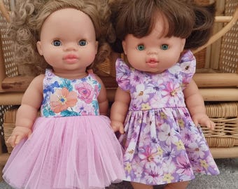 May include: Two dolls with brown hair and blue eyes. The left doll has curly hair and wears a floral bodice with a pink tulle skirt. The right doll has straight hair and wears a short-sleeved dress with a purple and white floral pattern.