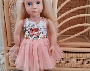 May include: A doll with long blonde hair and blue eyes wearing a sleeveless dress with a white bodice featuring a floral print of red roses and yellow daisies, paired with a layered peach-colored tulle skirt and light pink buckled shoes.