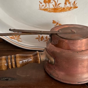 May include: A vintage copper pot with a wooden handle and a hinged lid. The pot has a tarnished finish and is in good condition.