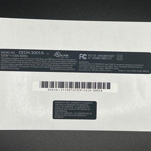 May include: A white label with black text and a barcode. The label includes the model number CECH-3001A, serial number CF430722329-CECH-3001A, and other technical specifications. A warning label is also present.