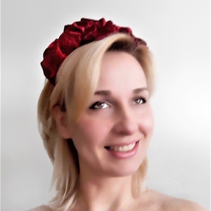 Puede incluir: Una diadema de terciopelo rojo con un dise&ntilde;o fruncido y plisado. La diadema la lleva una persona con el pelo rubio.