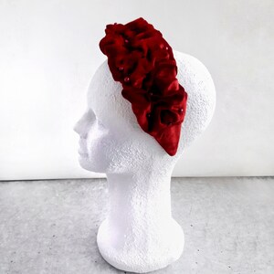 Puede incluir: Una diadema de terciopelo rojo con un dise&ntilde;o de volantes y peque&ntilde;os adornos de perlas.