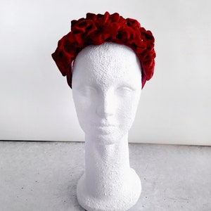 Puede incluir: Una diadema de terciopelo rojo con un dise&ntilde;o de volantes. La diadema est&aacute; en una cabeza de maniqu&iacute; blanca.