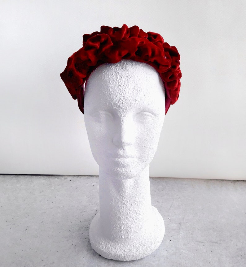 Puede incluir: Una diadema de terciopelo rojo con un dise&ntilde;o de volantes. La diadema est&aacute; en una cabeza de maniqu&iacute; blanca.