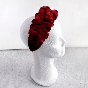 Puede incluir: Una diadema de terciopelo rojo con un dise&ntilde;o de volantes. La diadema est&aacute; decorada con peque&ntilde;as cuentas rojas.