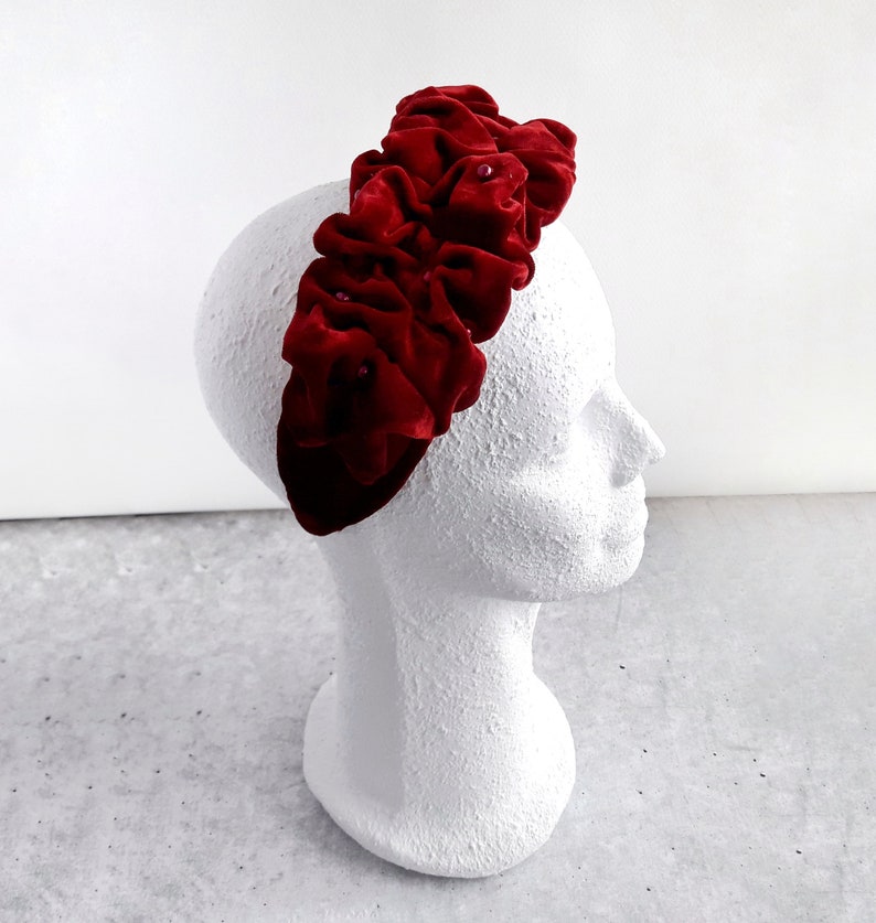 Puede incluir: Una diadema de terciopelo rojo con un dise&ntilde;o de volantes. La diadema est&aacute; decorada con peque&ntilde;as cuentas rojas.