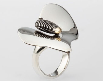 May include: A silver ring with a gold and black spiral design. The ring is shaped like a flower petal.