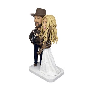 three-quarter view of the custom hunting wedding bobblehead, showing the detailed camouflage jackets and the man's rifle from a side angle on a clean white background.