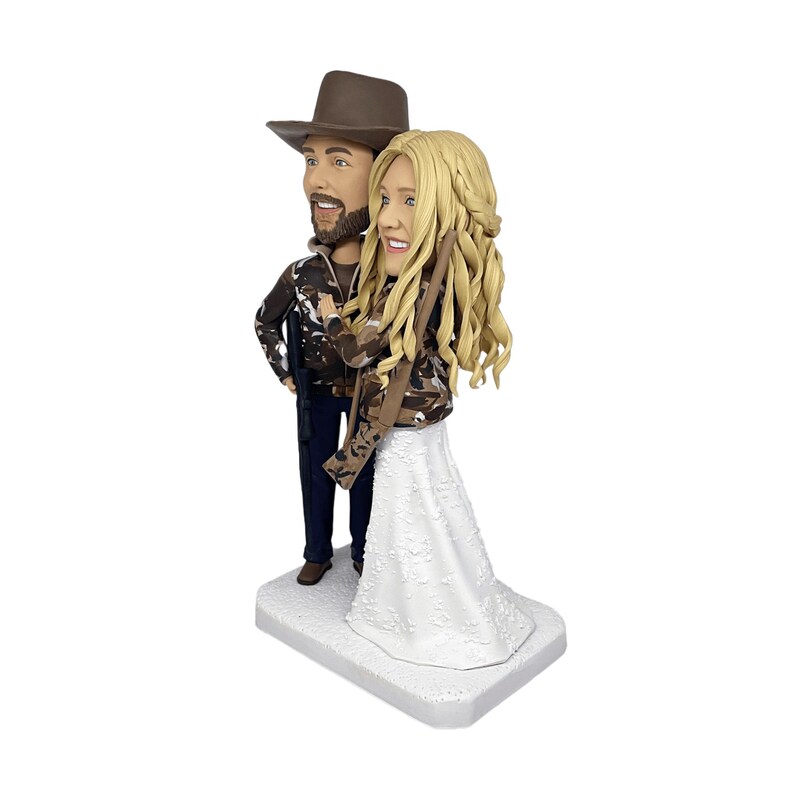 three-quarter view of the custom hunting wedding bobblehead, showing the detailed camouflage jackets and the man's rifle from a side angle on a clean white background.