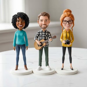 Könnte beinhalten: Drei Wackelkopf-Figuren. Eine hat dunkles, lockiges Haar, einen blauen Pullover und Jeans. Die zweite hält eine Gitarre und trägt ein kariertes Hemd und eine grüne Hose. Die dritte hat rotes Haar, eine Brille, einen gelben Kapuzenpullover, eine schwarze Hose und eine Kamera.