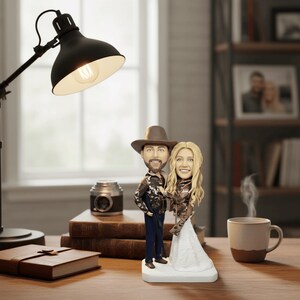 styled product photo of the hunter couple bobblehead on a rustic wooden desk, with a lit lamp, books, and a coffee mug in the background, showing the figurine as a decorative gift.