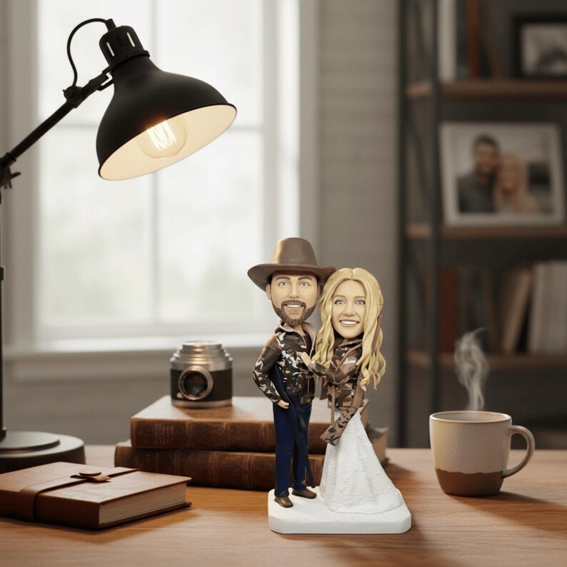 styled product photo of the hunter couple bobblehead on a rustic wooden desk, with a lit lamp, books, and a coffee mug in the background, showing the figurine as a decorative gift.