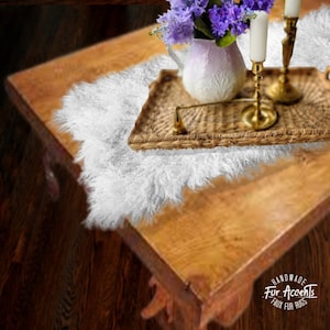 May include: A white faux fur rug on a wooden table with a wicker tray, two gold candle holders, and a white pitcher with purple flowers. The text "Handmade Fur Accents Faux Fur Rugs" is visible in the bottom right corner of the image.