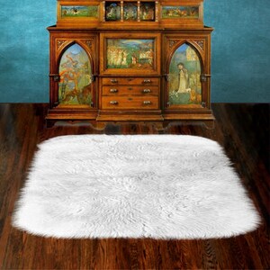May include: A white fluffy rug with a long pile, placed on a wooden floor in front of an antique wooden cabinet with intricate carvings and painted panels.