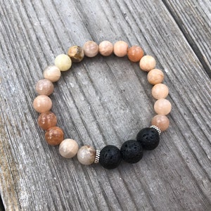 May include: A bracelet made of light orange, peach, and white beads with two black lava rock beads and silver spacers.