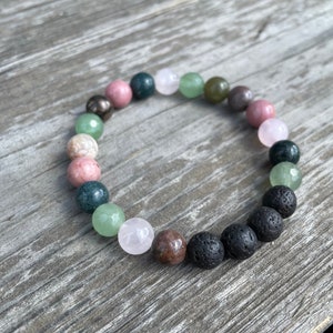 May include: A bracelet made with various coloured beads, including green, pink, and black. The bracelet is made with natural stones and lava beads.