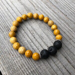 May include: A yellow and black beaded bracelet with a silver accent. The bracelet is made with round beads and has a natural stone look.