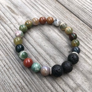 May include: A bracelet made of various coloured gemstone beads and black lava beads. The bracelet features round beads in shades of green, red, brown, and grey, strung together with a silver-coloured spacer.
