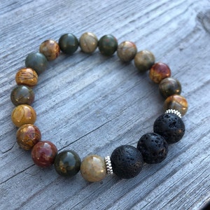 May include: A multi-coloured gemstone bracelet with black lava beads. The bracelet has a mix of green, brown, and red stones.
