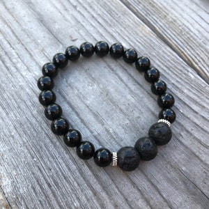May include: Black beaded bracelet with three lava rock beads. The bracelet is made with black onyx beads and silver spacers.