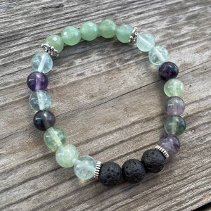 May include: A green and purple gemstone bracelet with black lava rock beads and silver accents.