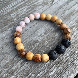 May include: A bracelet made of wooden beads in shades of brown and pink, with black lava rock beads at one end.