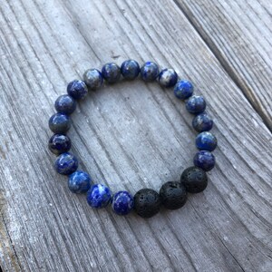 May include: A blue and black beaded bracelet with lava rock beads. The bracelet is made with lapis lazuli and black lava rock beads.