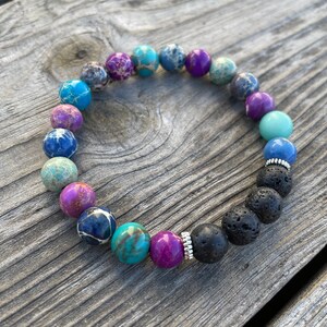 May include: A colourful beaded bracelet with a mix of blue, purple, turquoise, and pink stones. The bracelet also features black lava rock beads and a silver spacer bead.