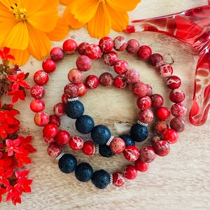 May include: Two bracelets made of red jasper beads and black lava beads. The bracelets are stacked on top of each other.