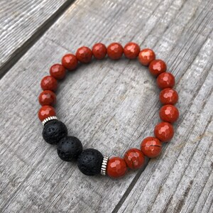 May include: Red and black beaded bracelet with silver accents. The bracelet is made with red gemstone beads and black lava rock beads.