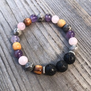 May include: A bracelet made with various stones, including amethyst, rose quartz, lava rock, and wood beads. The bracelet has a silver spacer bead.