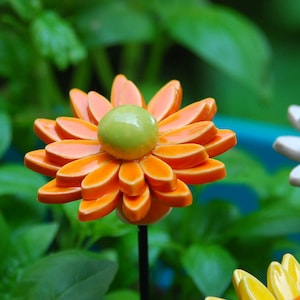 K&ouml;nnte beinhalten: Drei Keramik-Blumen-Dekorationen. Die erste Blume ist orange mit einer gr&uuml;nen Mitte. Die zweite Blume ist wei&szlig; mit einer gelben Mitte. Die dritte Blume ist gelb mit einer orangenen Mitte.