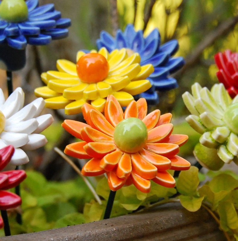 K&ouml;nnte beinhalten: Eine Sammlung von Keramikblumen in verschiedenen Farben, darunter Blau, Gelb, Orange, Wei&szlig; und Gr&uuml;n. Die Blumen sind zu einem Strau&szlig; angeordnet und haben ein realistisches Aussehen.