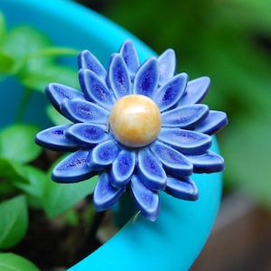 K&ouml;nnte beinhalten: Eine blaue Keramikblume mit gelber Mitte, die auf einem blauen Topf sitzt.