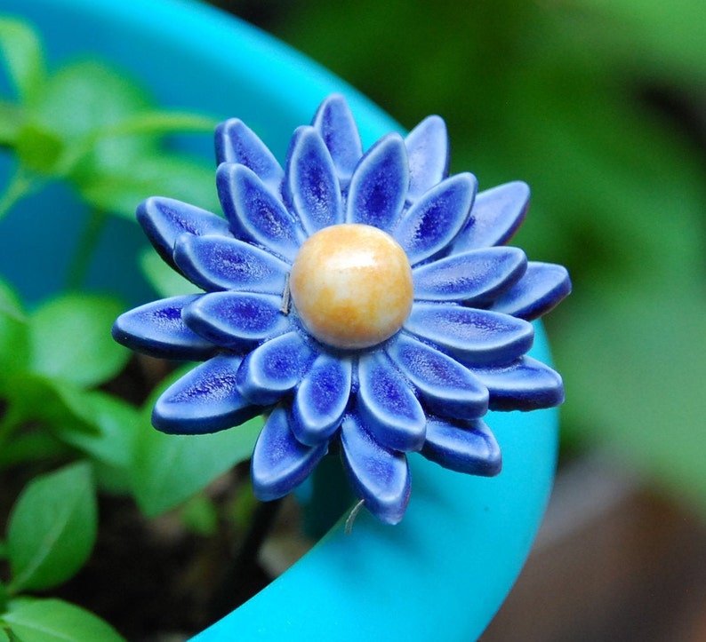 K&ouml;nnte beinhalten: Eine blaue Keramikblume mit gelber Mitte, die auf einem blauen Topf sitzt.