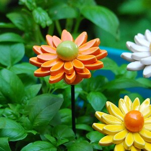 K&ouml;nnte beinhalten: Drei Keramik-Blumen-Gartenstecker. Die Blumen sind orange, gelb und wei&szlig;. Die orange Blume hat eine gr&uuml;ne Mitte. Die gelbe Blume hat eine orange Mitte. Die wei&szlig;e Blume hat eine gelbe Mitte.