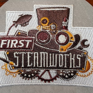 Peut inclure: Patch brodé avec un design steampunk. Il présente un chapeau haut de forme brun avec des engrenages et des lunettes, une clé à molette et les mots "FIRST STEAMWORKS".
