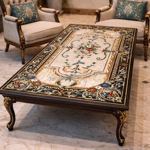 Könnte beinhalten: Ein rechteckiger Couchtisch mit einem dunkelbraunen Holzrahmen und verzierten goldenen Akzenten. Die Tischplatte hat eine cremefarbene Marmoreinlage mit einem floralen Mosaikdesign in verschiedenen Farben. Der Tisch ist etwa 152 cm lang und 76 cm breit.