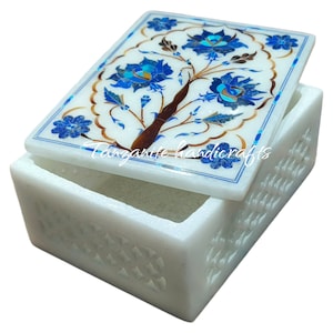 Könnte beinhalten: Weiße Marmor-Schmuckschatulle mit einem floralen Design auf dem Deckel. Der Deckel ist mit blauen und goldenen Blumen und Blättern verziert. Die Schachtel ist mit einem geometrischen Muster verziert.