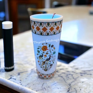 Könnte beinhalten: Eine weiße Marmorvase mit blauem Innenraum und aufwendigen floralen und Vogelmotiven. Die Vase ist mit bunten Steinen verziert und trägt den Schriftzug "Tanzanite handicrafts" an der Seite.