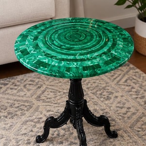 Könnte beinhalten: Ein runder Beistelltisch mit einer leuchtend grünen Tischplatte im Malachit-Muster mit konzentrischen kreisförmigen Designs. Der Tisch wird von einem schwarzen Säulenfuß mit drei verzierten, geschwungenen Beinen getragen.