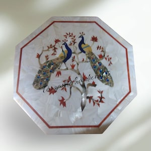 May include: Octagonal white marble table top with a red border. The table top features an inlaid design of two peacocks on a tree with red leaves. The text "Tanzanite handicrafts" is visible in the lower centre of the table top.