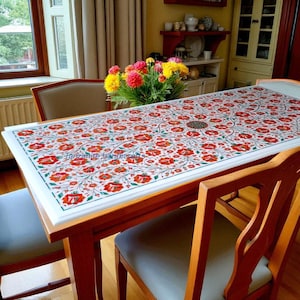 Könnte beinhalten: Ein rechteckiger Esstisch mit einer weißen Marmorplatte mit einem Blumenmuster in Rot und Grün. Der Tisch wird von einem Holzrahmen getragen und von Holzstühlen umgeben. Der Text "Tanzanite handicrafts" ist sichtbar.